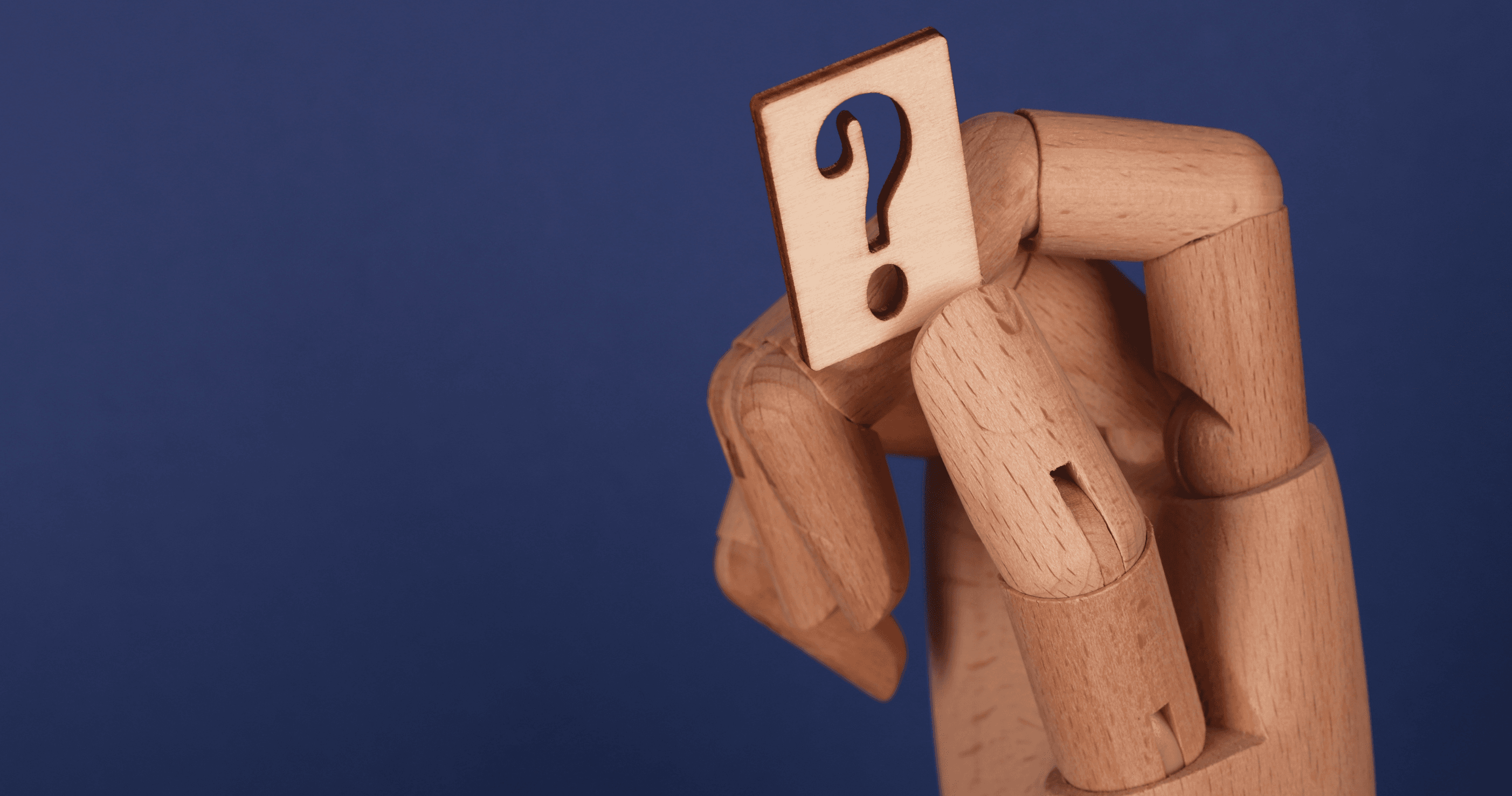 Wooden mannequin holding a square tile with a question mark against a blue background.