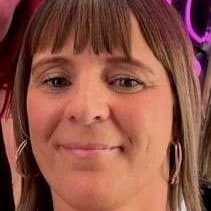 A woman with straight brown hair and bangs, wearing hoop earrings, smiles at the camera.