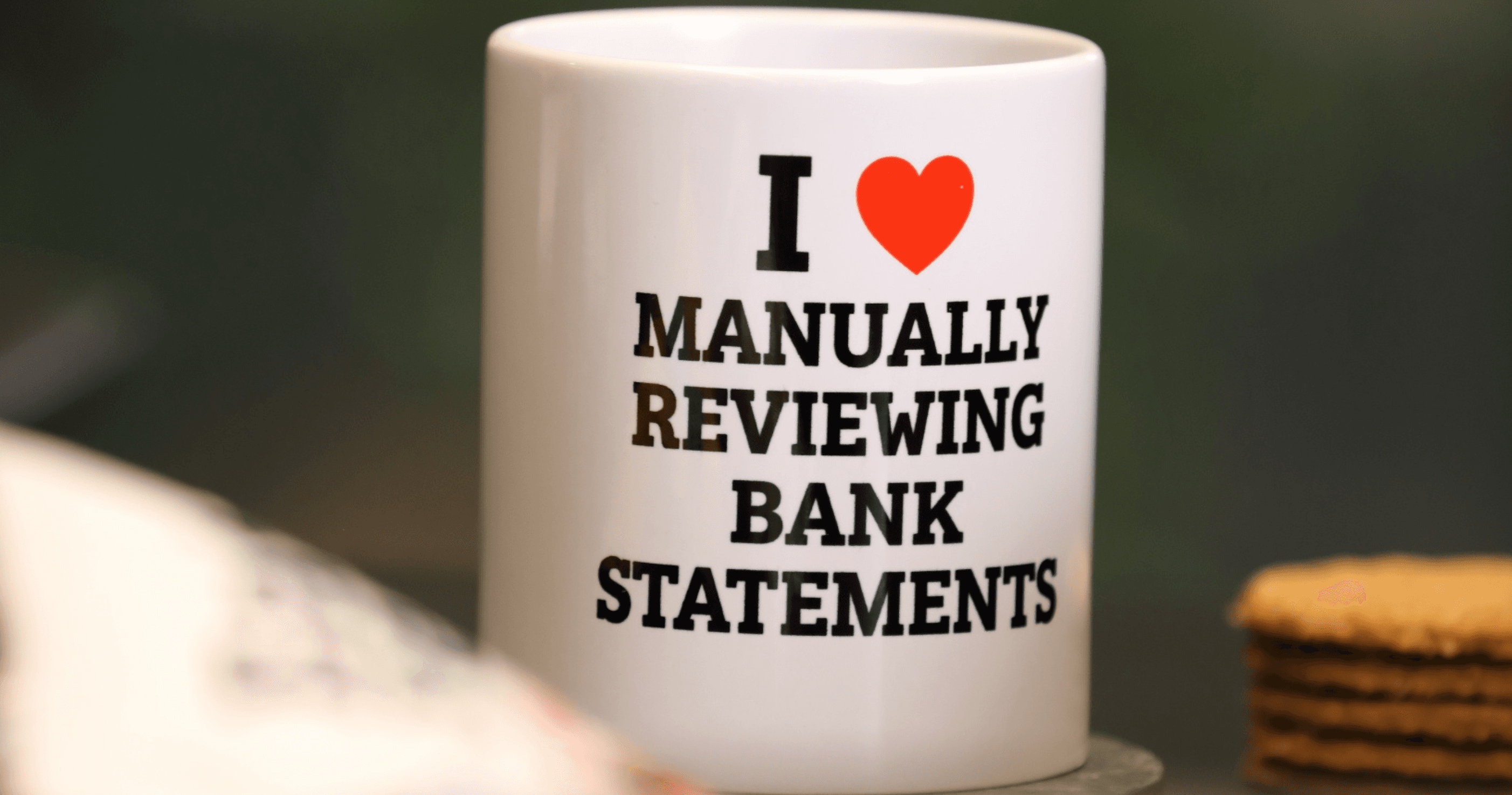White mug with black text: "I ♥ MANUALLY REVIEWING BANK STATEMENTS." A stack of cookies is visible in the background.
