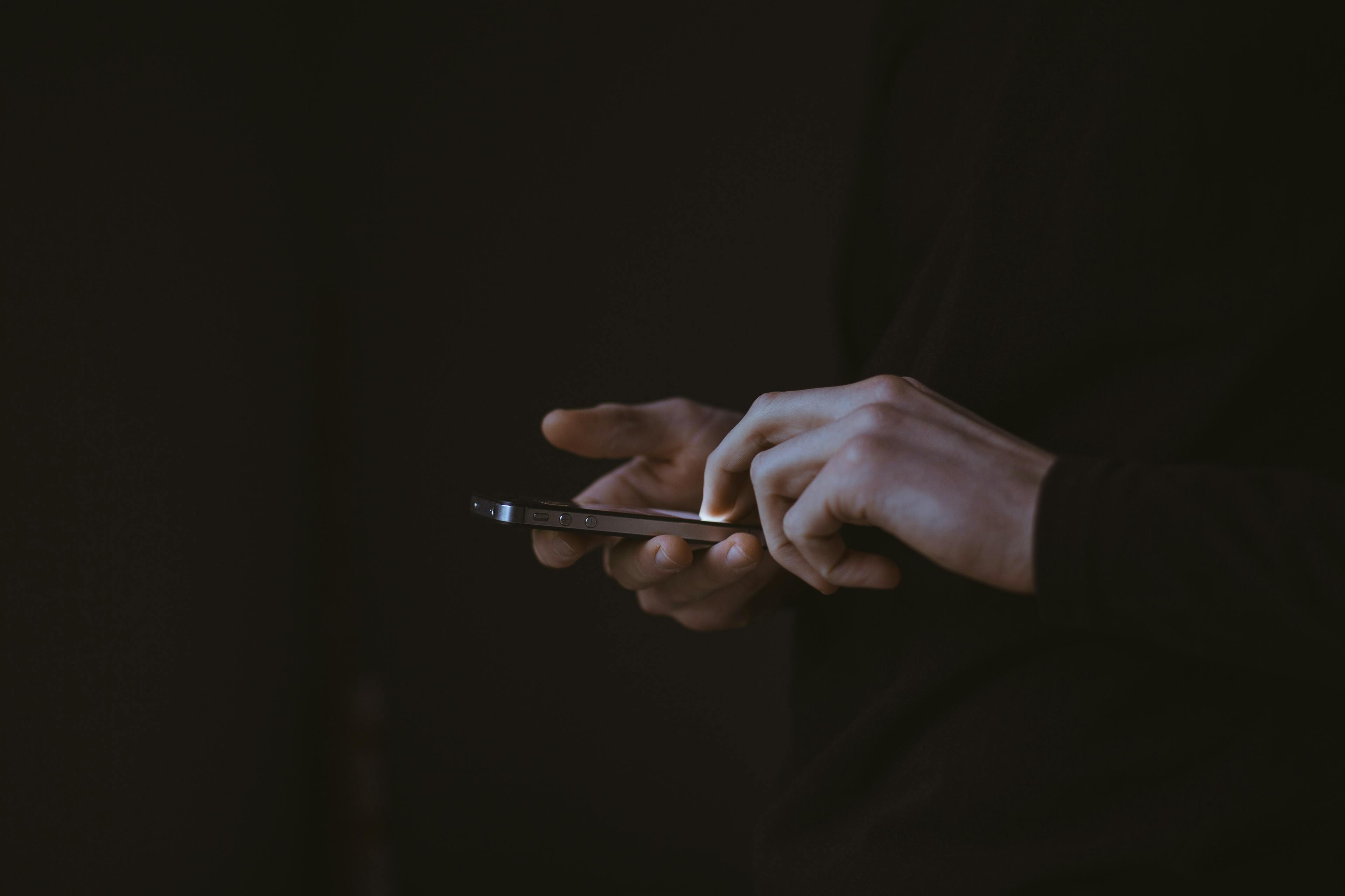 image close up of a person's hands using their phone against a dark background